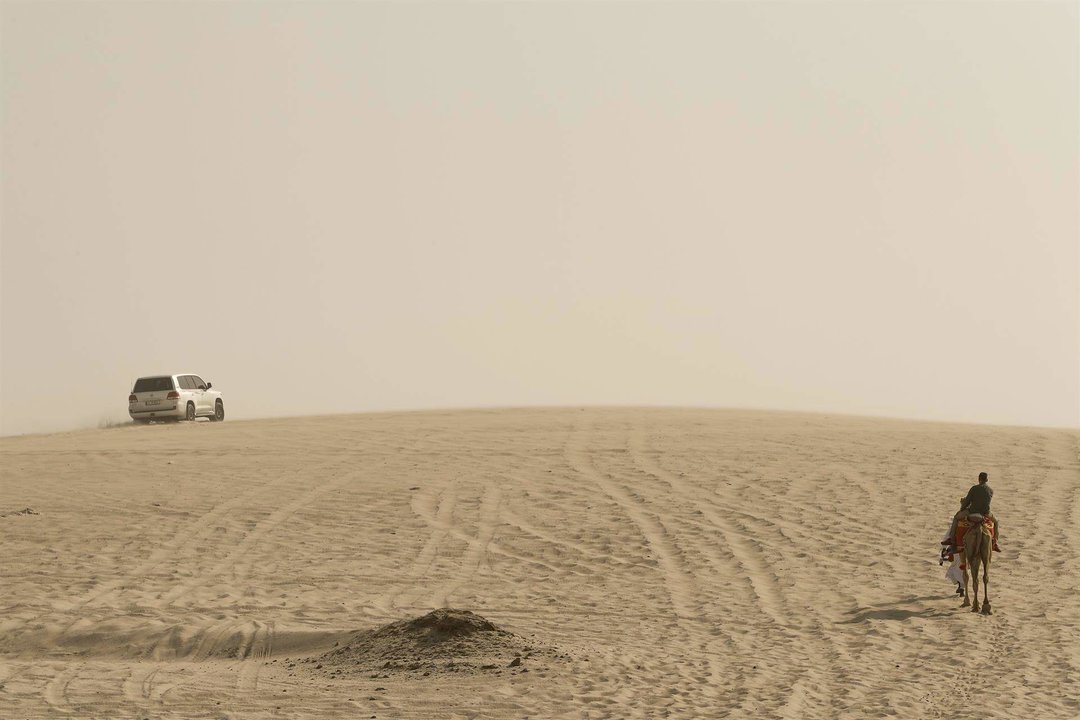 GRAF5287. DOHA, 18/10/2022.- Un turista en camello y un todoterreno se adentran en el desierto de Catar en una imagen tomada el 16/09/2022. Observar la inmensidad del desierto blanco y su rojo atardecer, sentir  la adrenalina al recorrer sus dunas en 4x4 y sorprenderte con un mar en medio de la arena, son tan solo algunas de las maravillas que esconde el desierto catarí y visita obligada para todos los que acudan al Mundial de Qatar 2022. EFE/ Alberto Estevez